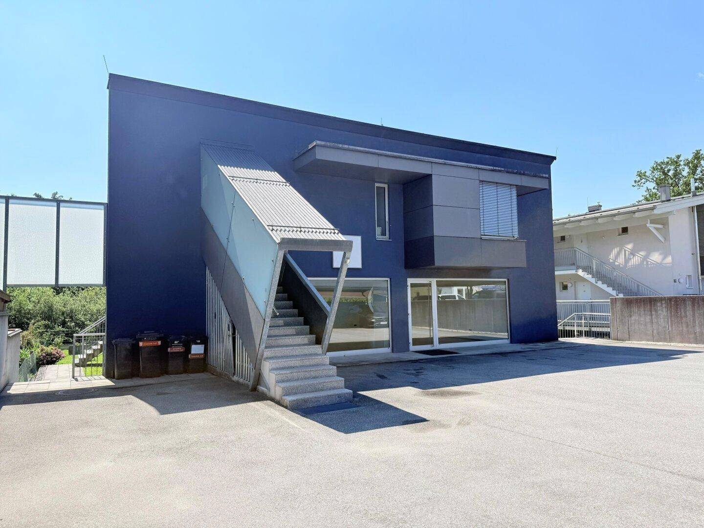Moderne Geschäftsfassade mit auffälliger Treppenkonstruktion und Parkplätzen.