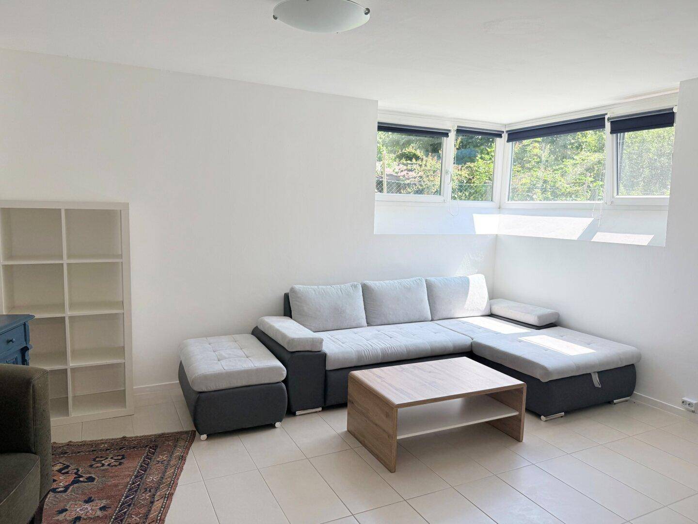 Gemütliches Wohnzimmer mit Sofa, Couchtisch und großen Fenstern.