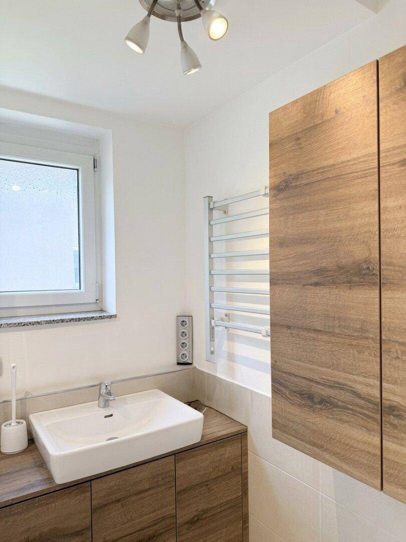 Modernes Badezimmer mit Holzschränken, Waschbecken und beheiztem Handtuchhalter.
