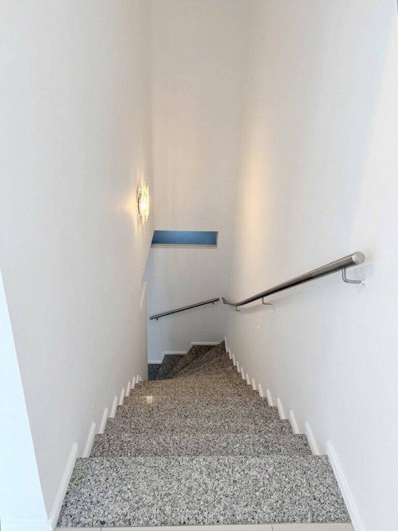 Treppenhaus mit Granitstufen und modernem Edelstahlgeländer in hellem Ambiente.