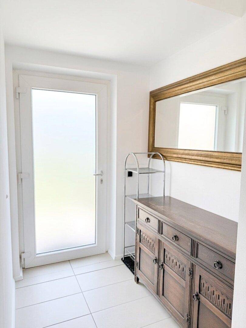 Heller Flur mit Fliesenboden, einer Holztruhe und einem großen Wandspiegel.