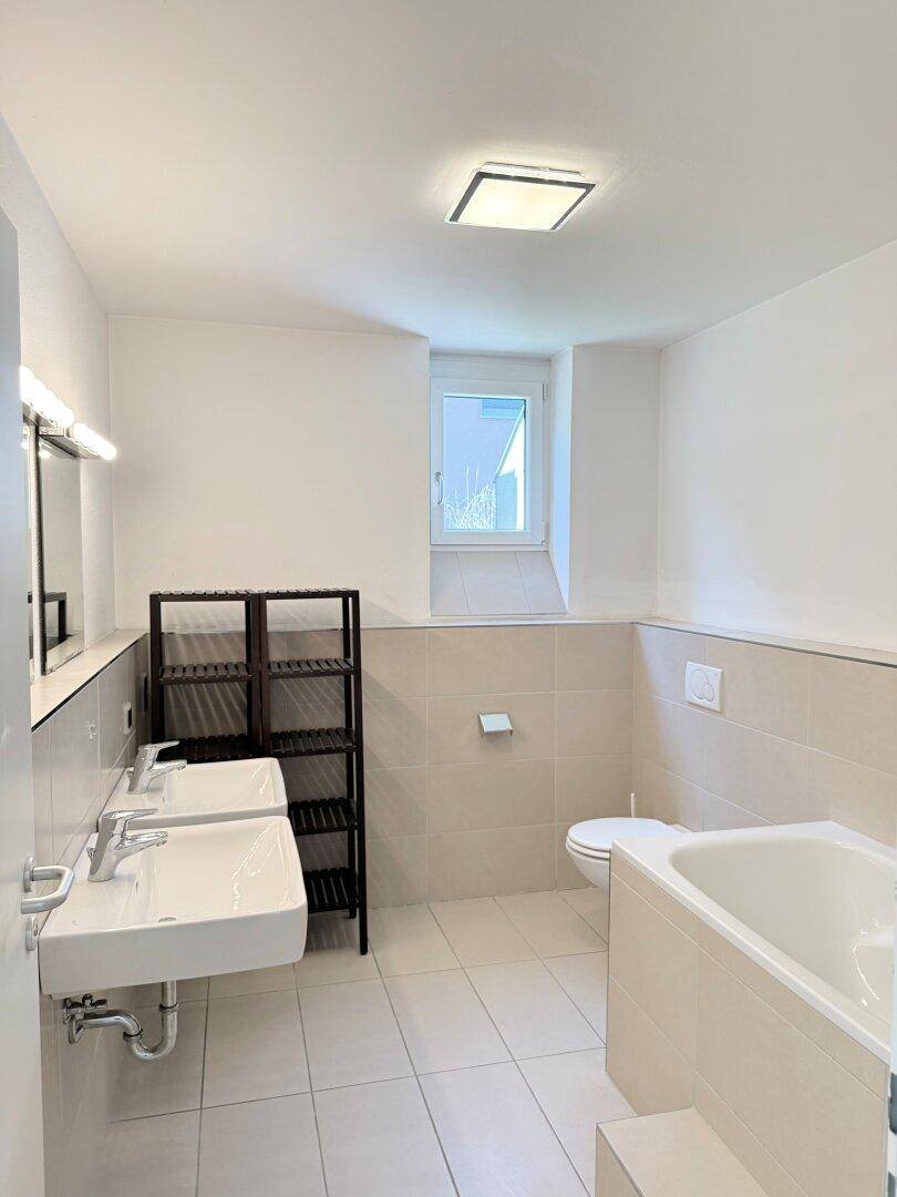 Geräumiges Badezimmer mit Doppelwaschbecken, Badewanne und Fenster.