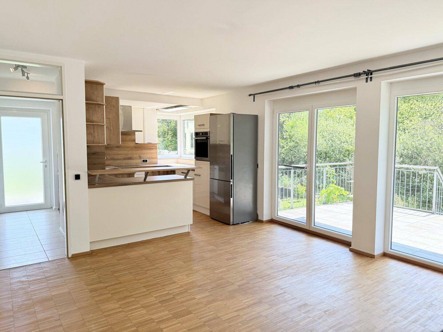 Heller offener Wohnbereich mit Parkettboden, integrierter Küche und Zugang zur Terrasse.