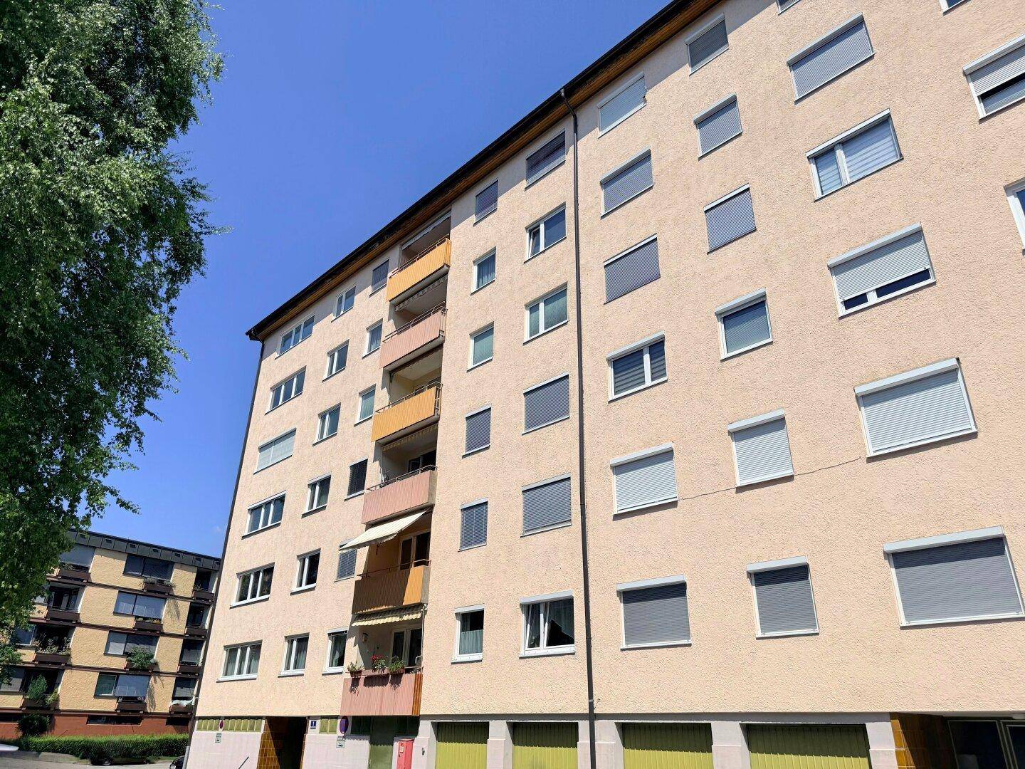 Mehrstöckiges Wohngebäude mit beiger Fassade, vielen Fenstern und Balkonen unter blauem Himmel.