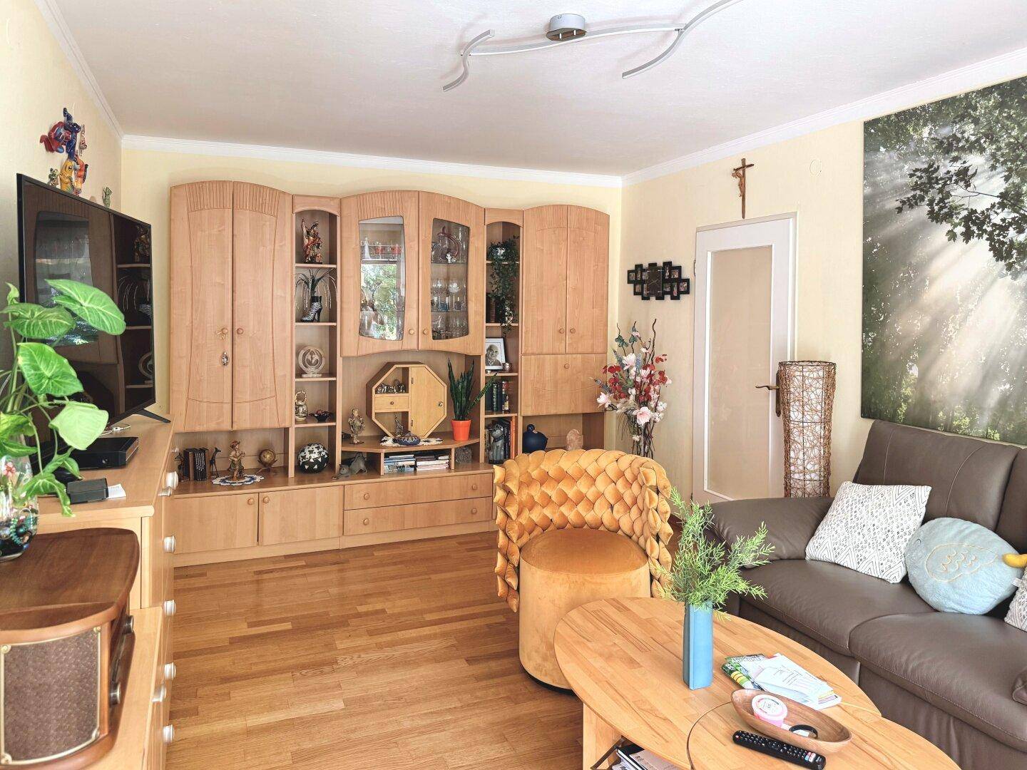 Gemütliches Wohnzimmer mit heller Holzschrankwand, beigem Sofa und Parkettboden.