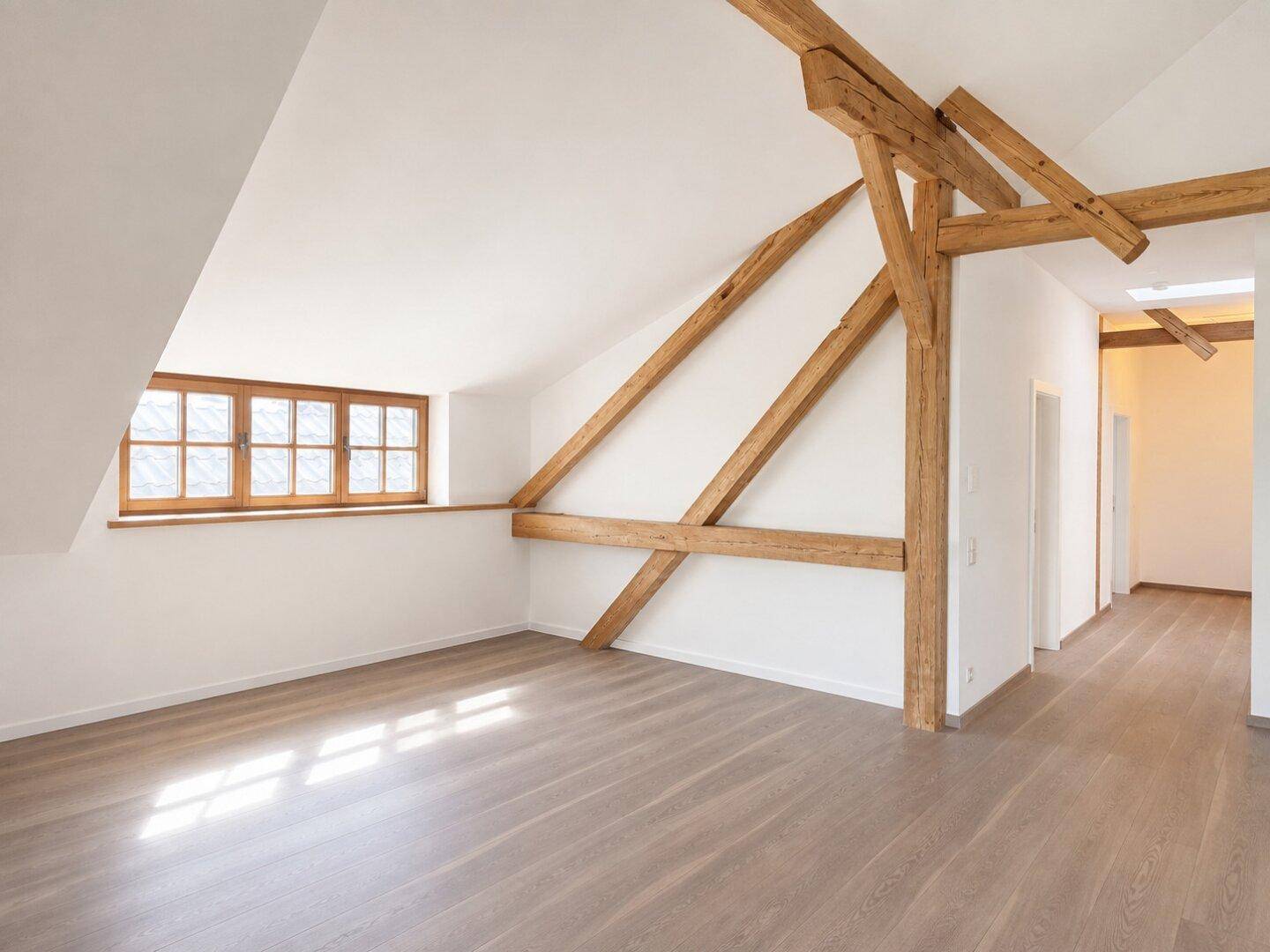 Heller Raum im Dachgeschoss mit sichtbaren Holzbalken und schrägen Wänden, bereit zur individuellen Gestaltung.