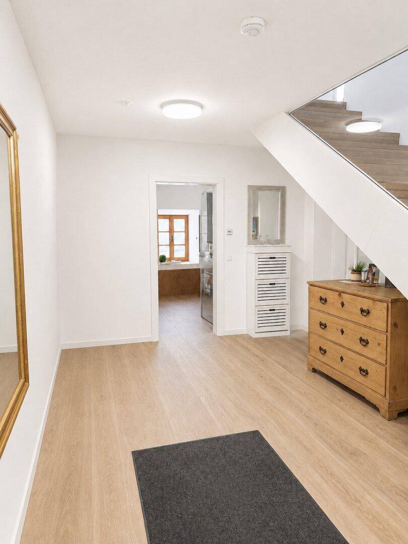 Einladender Eingangsbereich mit Holztreppe und hellem Laminatboden, der zu weiteren Räumen führt.