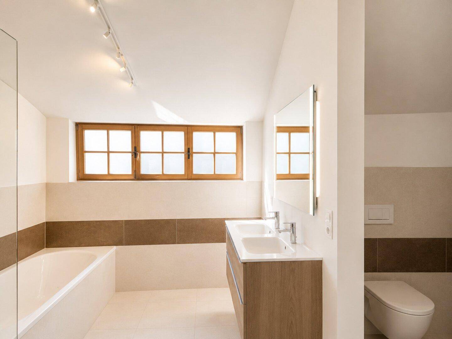 Geräumiges Badezimmer mit Badewanne, Doppelwaschbecken und großem Fenster für viel Tageslicht.