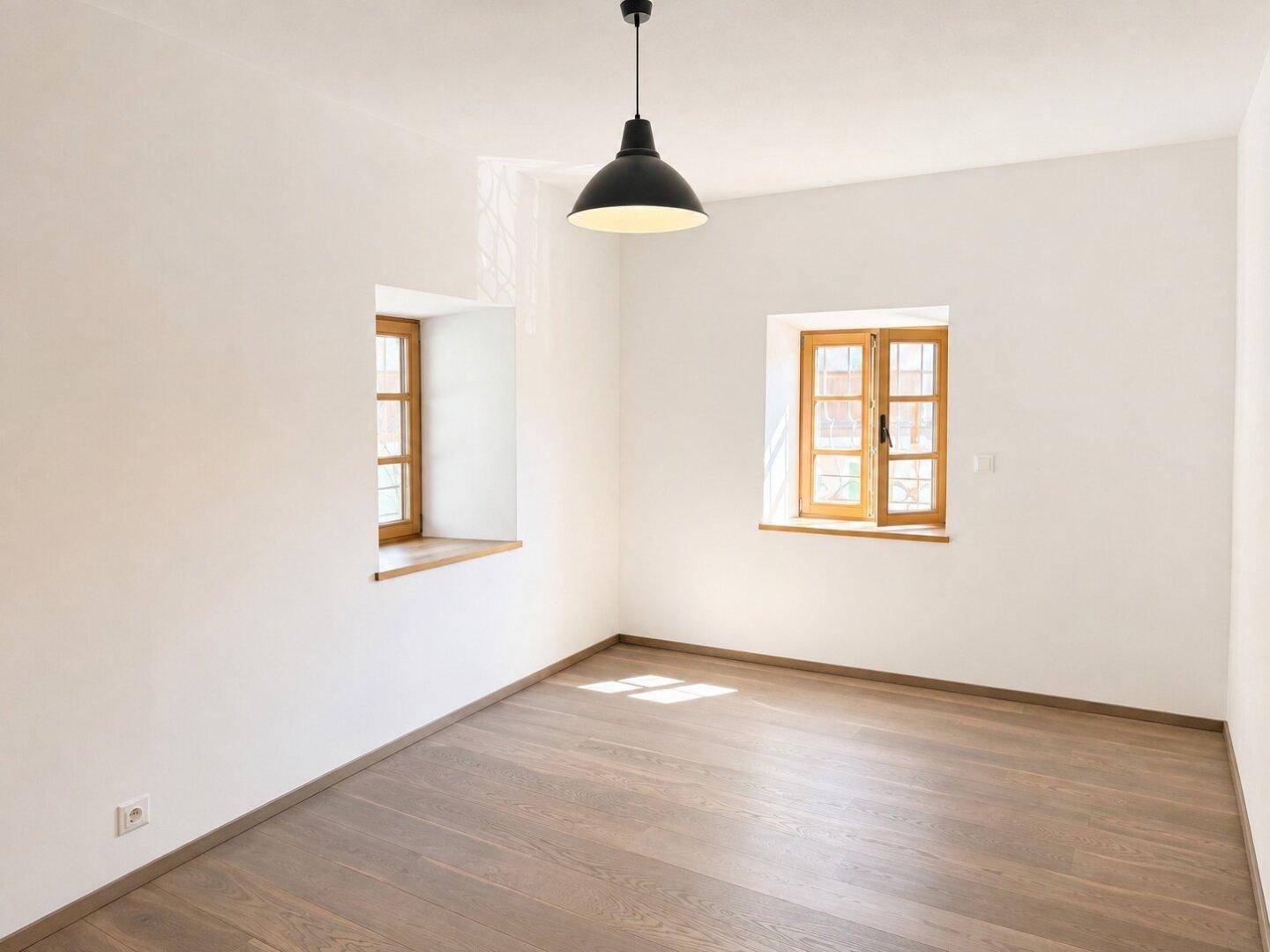 Leerer Raum mit zwei Fenstern und hellem Holzboden, ideal für Schlafzimmer oder Arbeitszimmer.