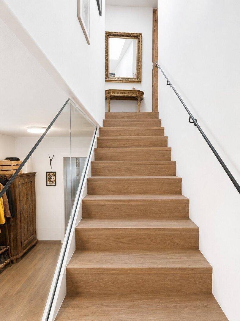 Elegante Holztreppe mit Glasgeländer und modernem Aufzug im Hintergrund, verbindet die Etagen.