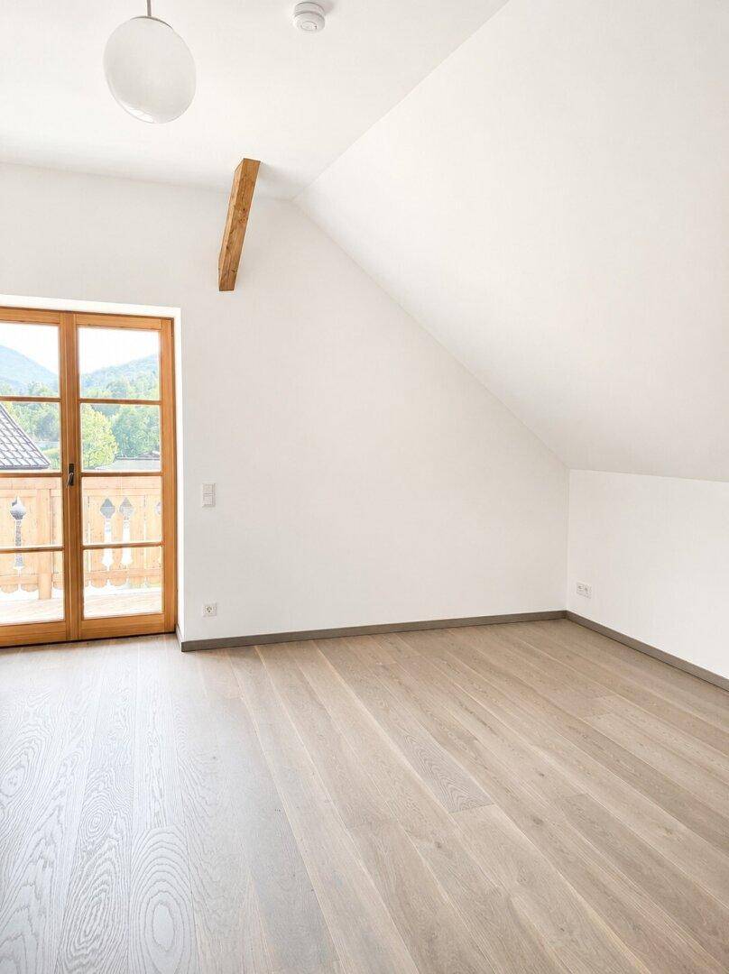 Helles Schlafzimmer im Dachgeschoss mit Zugang zu einem kleinen Balkon und Bergblick.