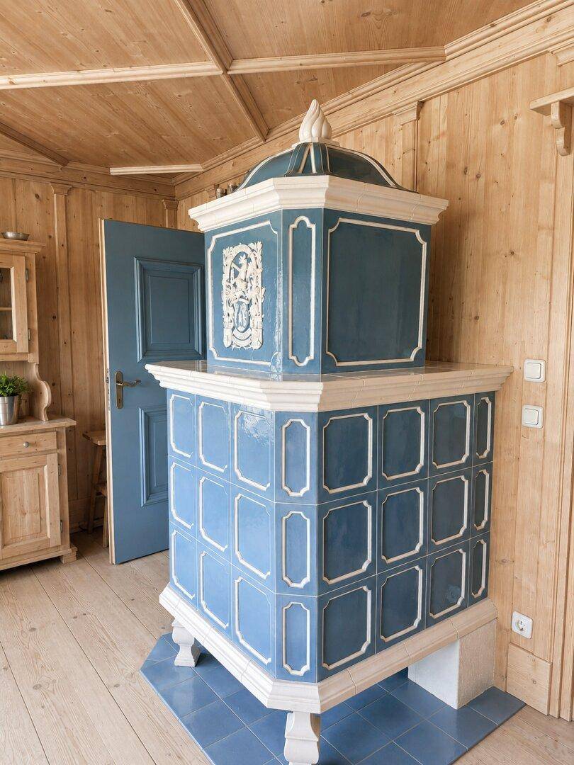 Detailansicht eines traditionellen blauen Kachelofens mit kunstvollen Verzierungen in einem Holzraum.