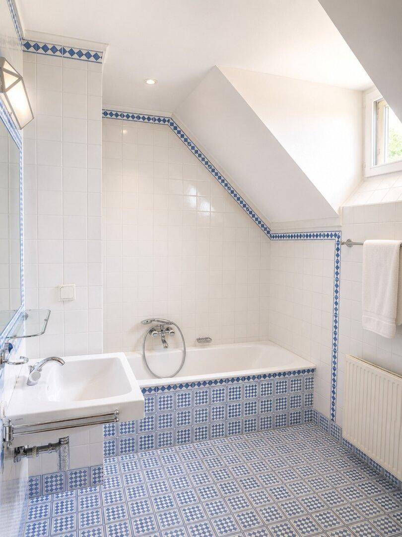 Badezimmer mit blauen und weißen Fliesen, Badewanne und Dachfenster für natürliches Licht.