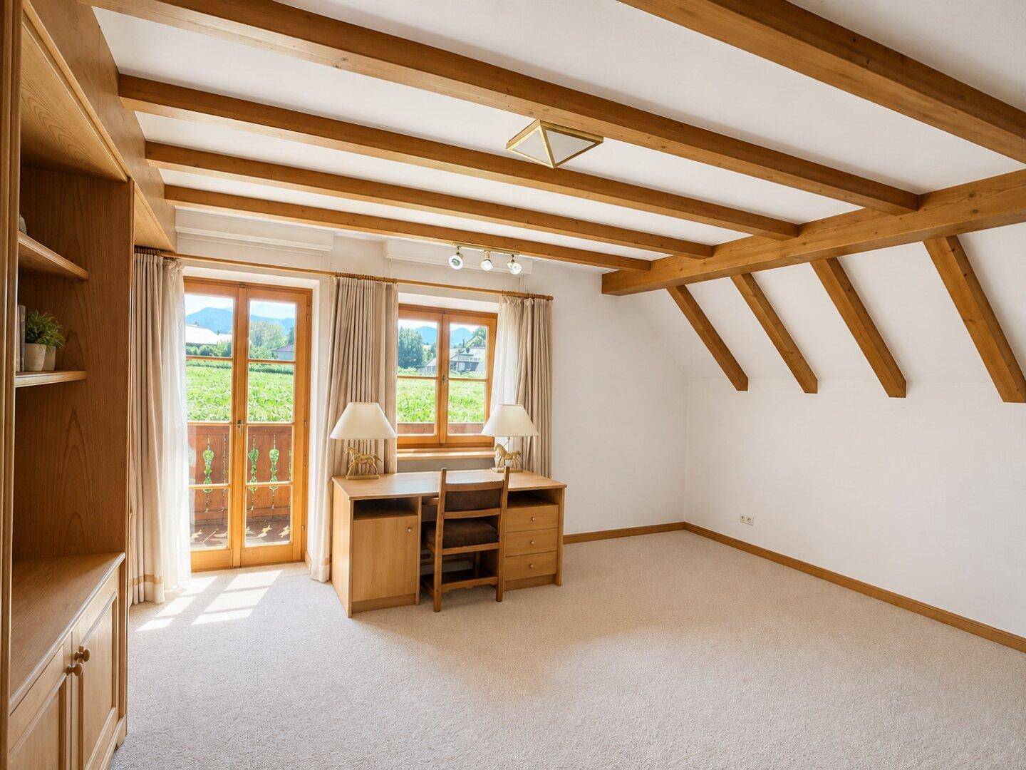 Helles Schlafzimmer mit Holzbalken, Teppichboden und Zugang zu einem Balkon mit Bergblick.