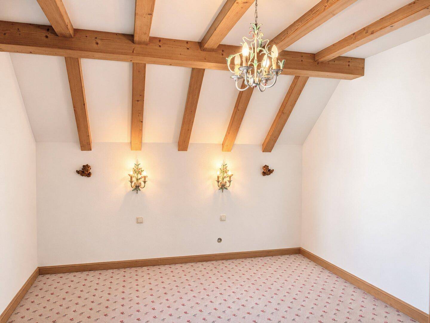 Schlafzimmer mit sichtbaren Holzbalken, Teppichboden und einem eleganten Kronleuchter.