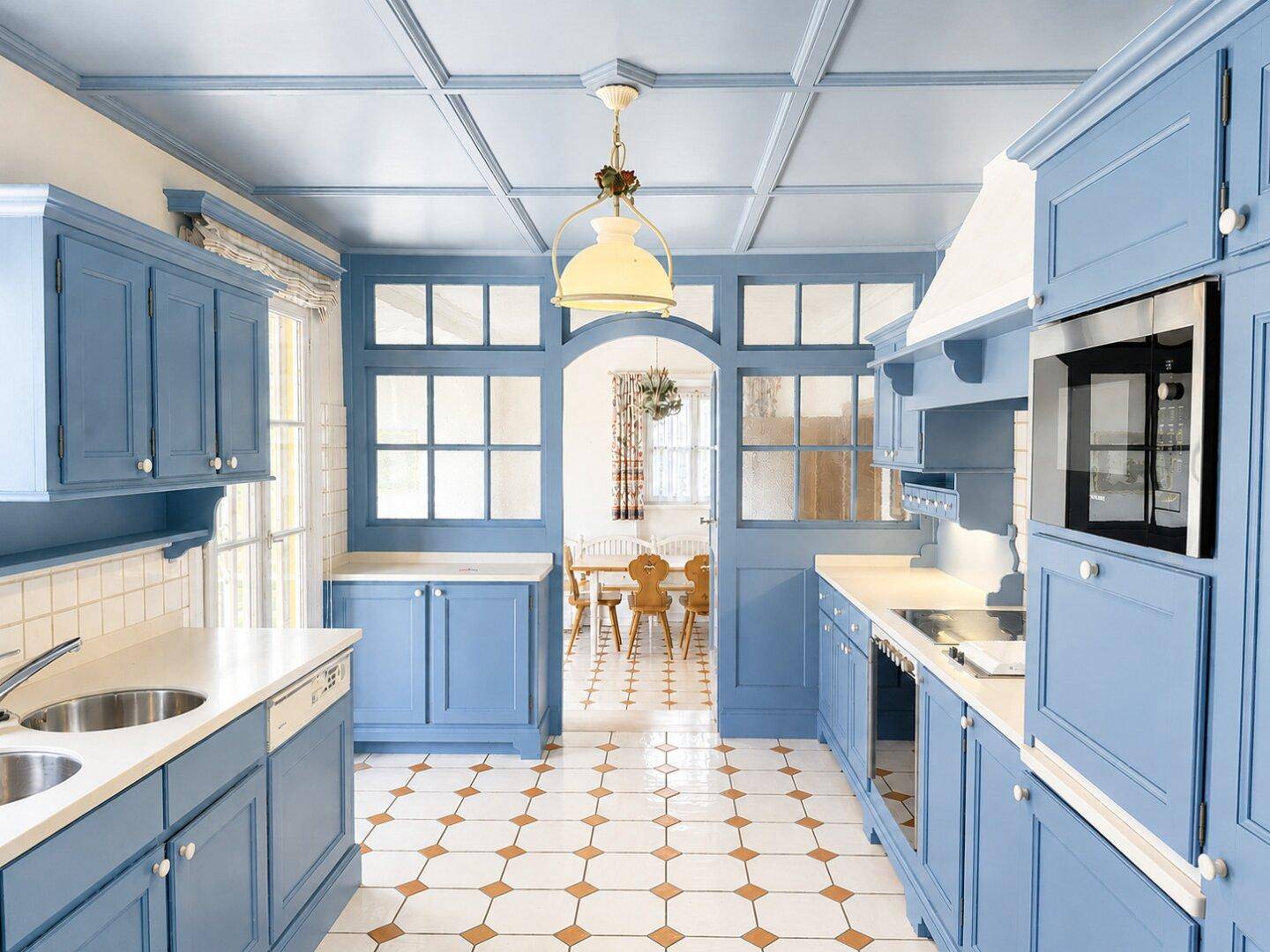 Helle Küche im Landhausstil mit blauen Schränken, gemusterten Fliesen und Blick in den Essbereich.