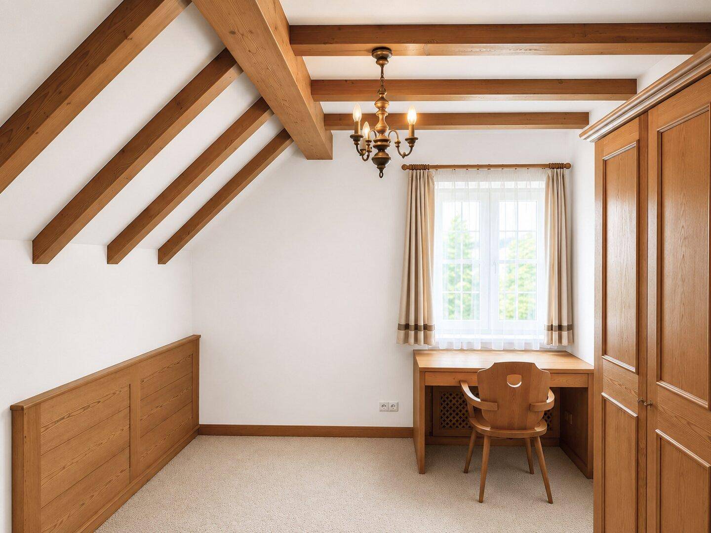 Dachgeschosszimmer mit Holzbalken, Teppichboden und einem Schreibtisch am Fenster.
