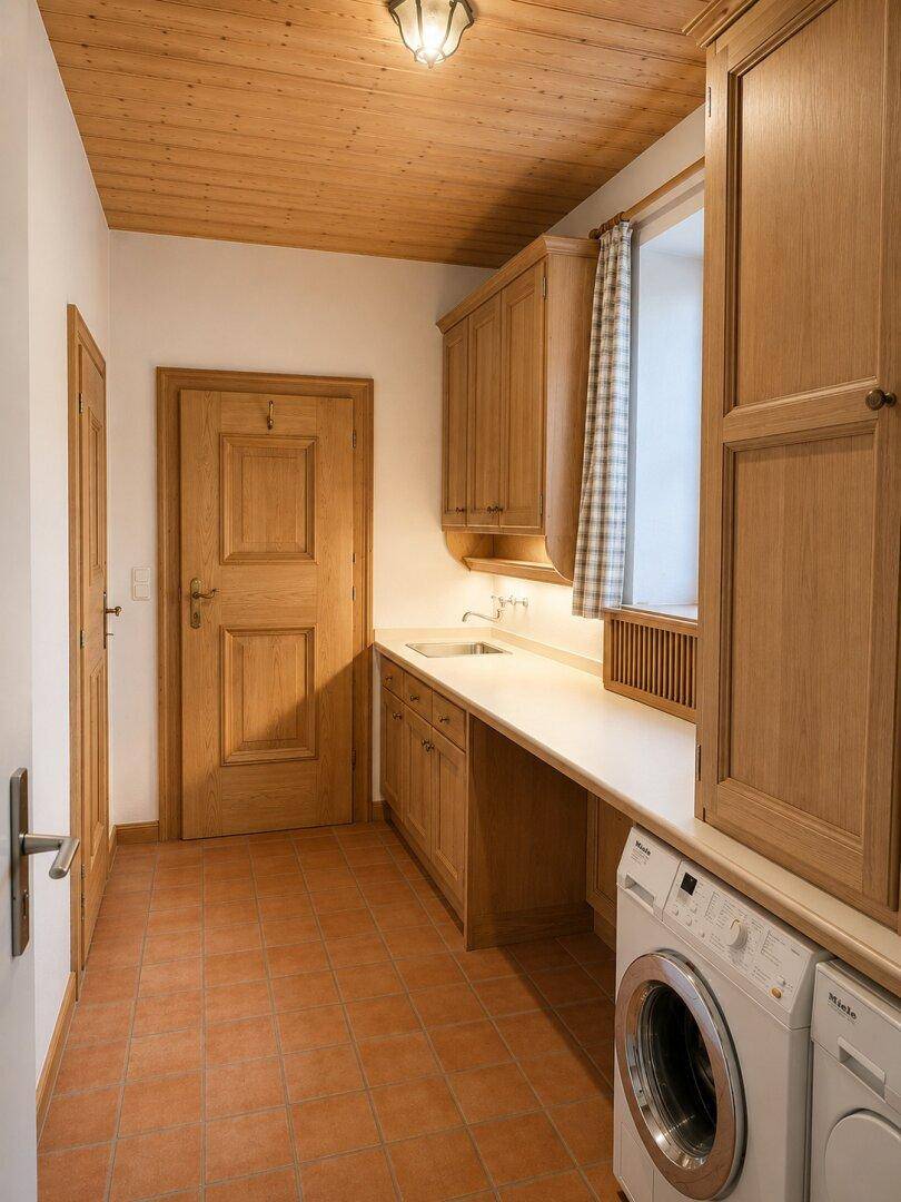 Praktischer Hauswirtschaftsraum mit Waschmaschine, Trockner und viel Stauraum in Holzschränken.