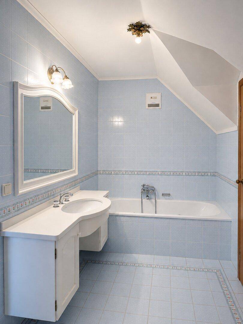 Hellblau gefliestes Badezimmer mit Badewanne, Waschtisch und Dachschräge, unter dem Dach gelegen.