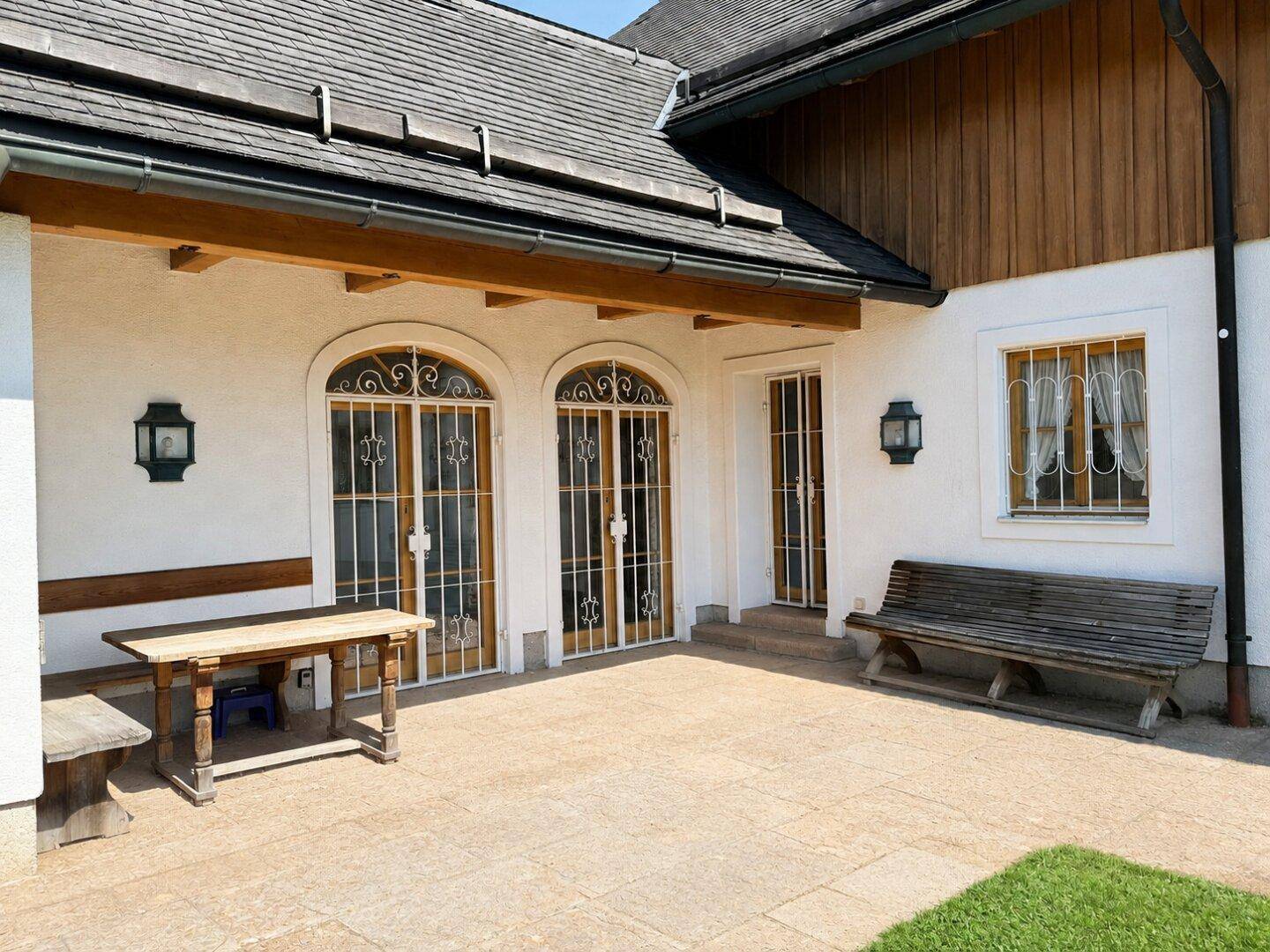 Gemütliche Steinterrasse mit Holzbänken und schmiedeeisernen Türen, ideal für entspannte Stunden.