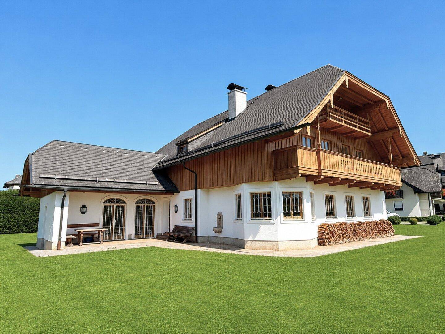 Traditionelles Landhaus mit Holzbalkonen und weißer Fassade, umgeben von einem gepflegten Rasen.