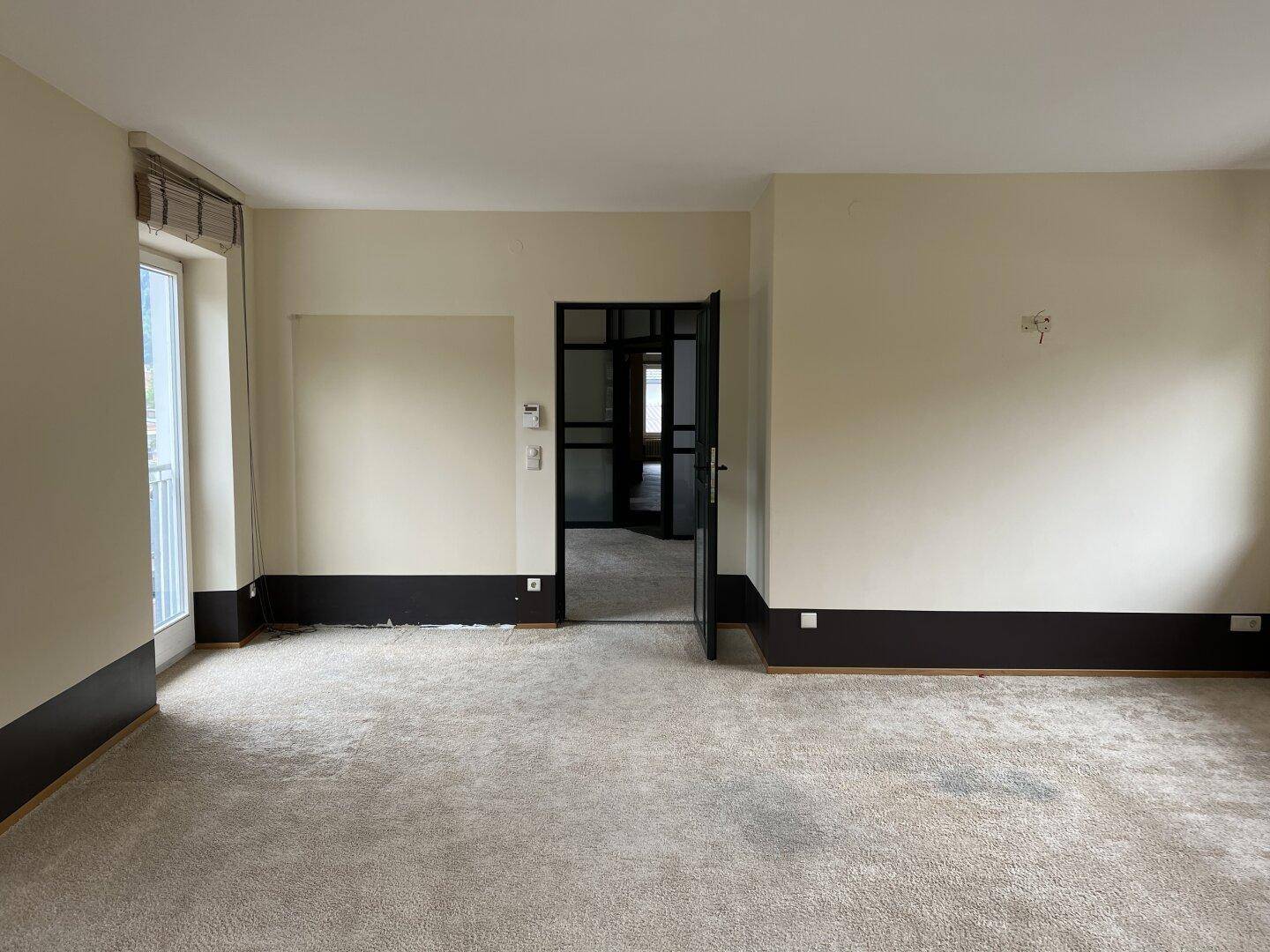 Geräumiges Zimmer mit Teppichboden, Zugang zum Balkon und einer modernen Glastür.