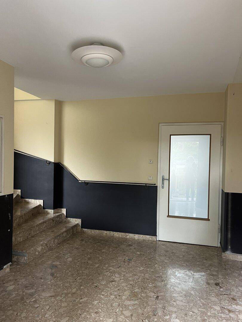 Treppenabsatz mit Terrazzoboden und einer Tür, die zu einer Wohnung führt, gut beleuchtet.
