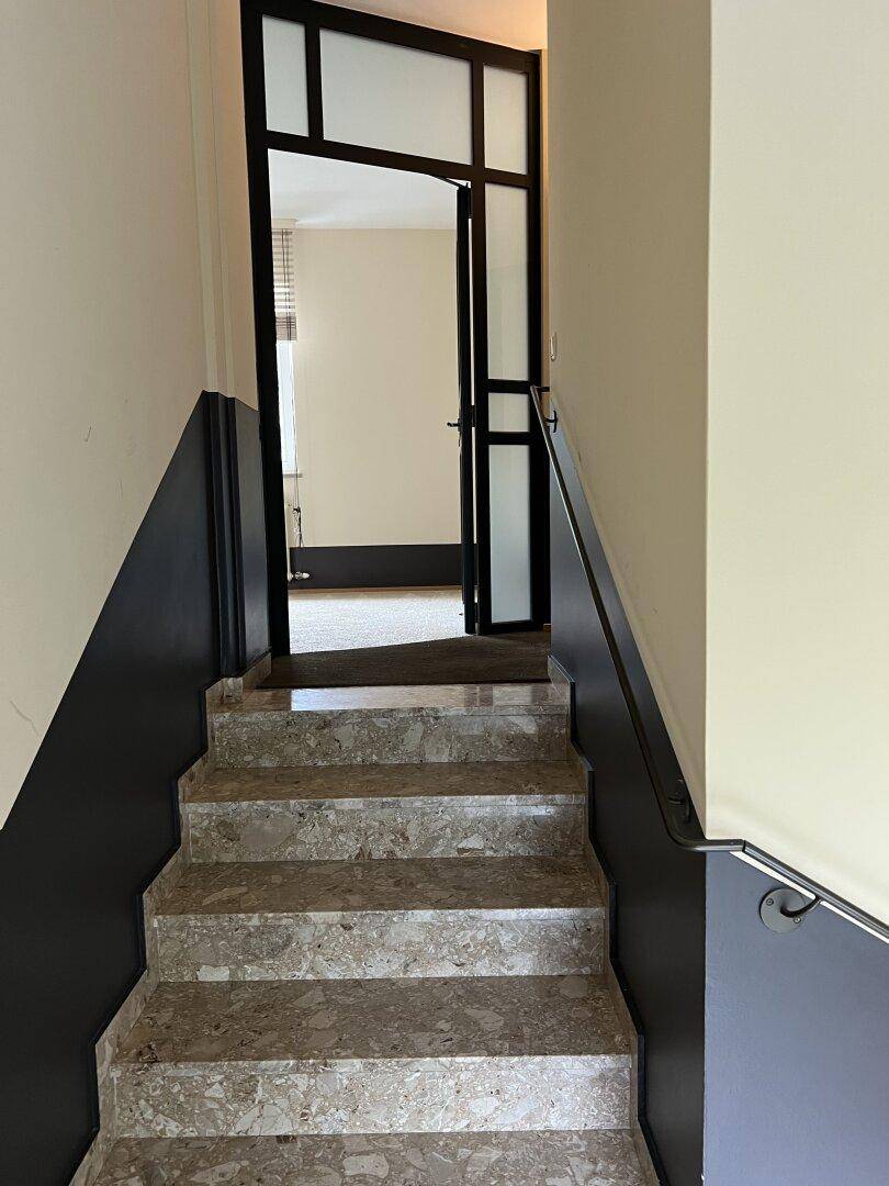 Treppenhaus mit Terrazzo-Stufen, das zu einer modernen Glastür führt, die den Zugang zum Wohnbereich ermöglicht.