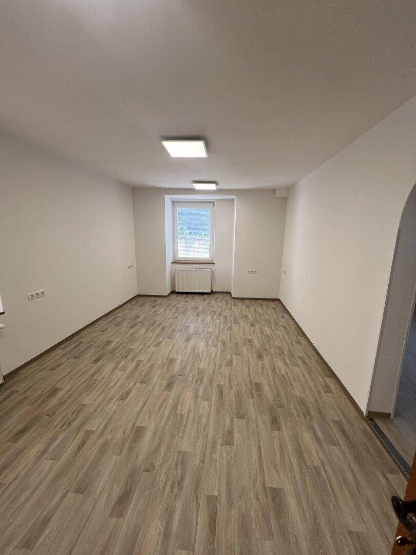 Geräumiges, leeres Zimmer mit Laminatboden, weißen Wänden und einem Fenster, bereit zur individuellen Gestaltung.