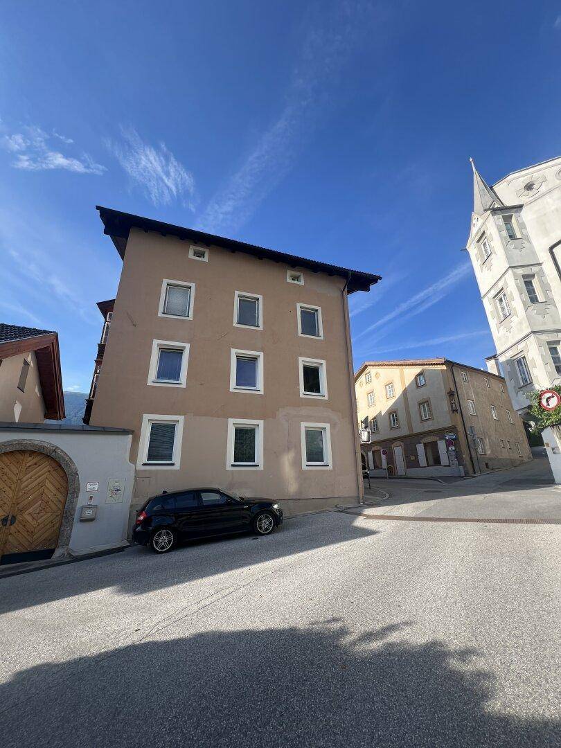 Ansicht eines historischen Gebäudes mit beiger Fassade und umliegender Straße unter klarem Himmel.