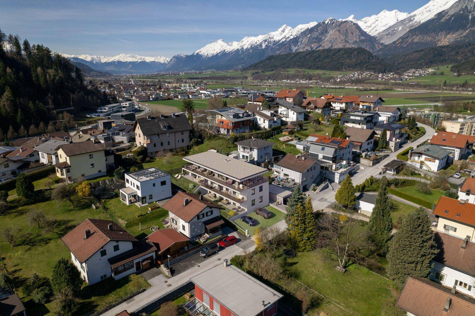 Luftaufnahme der Wohngegend mit dem modernen Gebäude und umliegender Berglandschaft unter blauem Himmel.