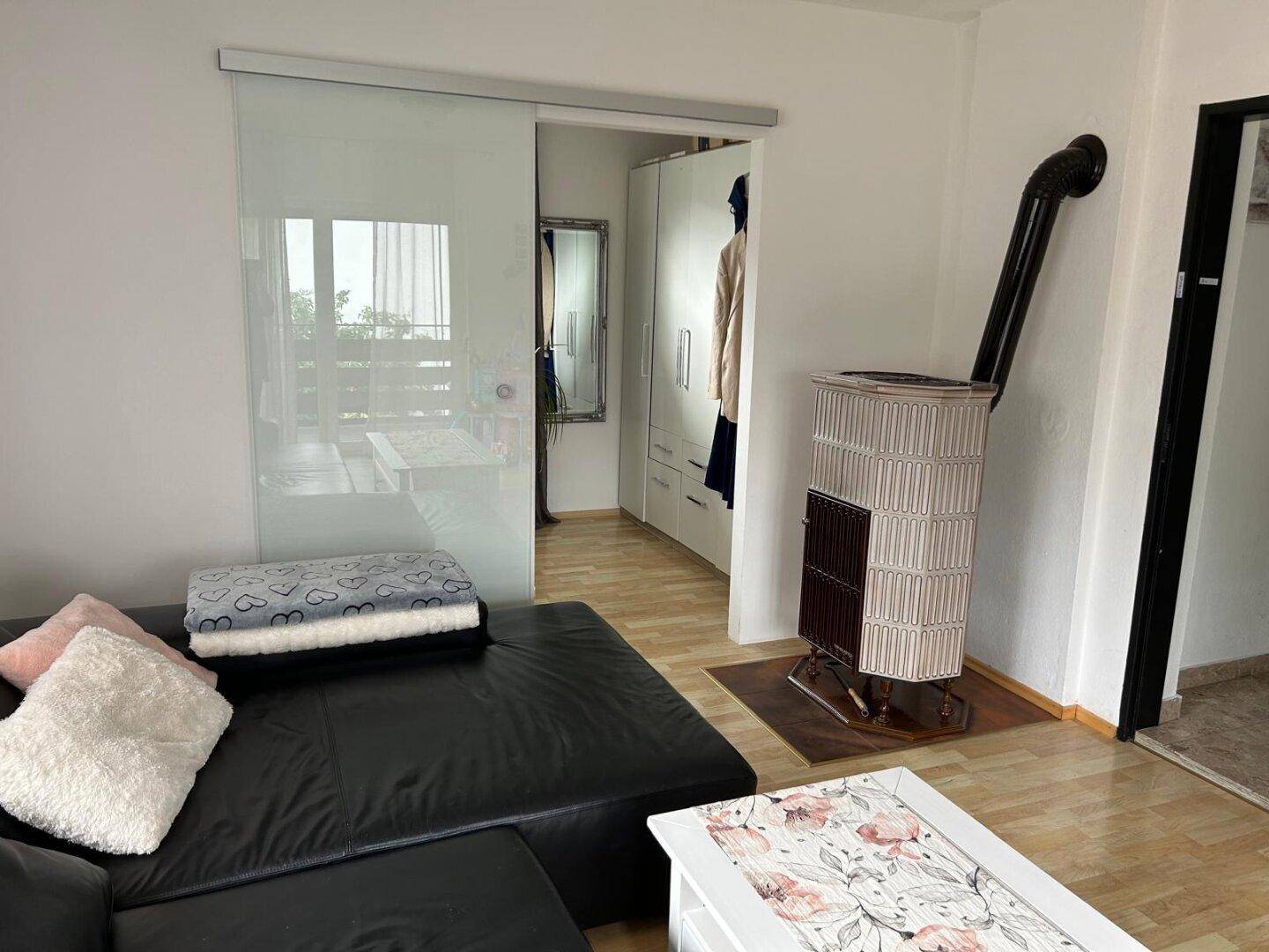 Gemütliches Wohnzimmer mit Kaminofen, Ledersofa und Schiebetür zu einem weiteren Raum.