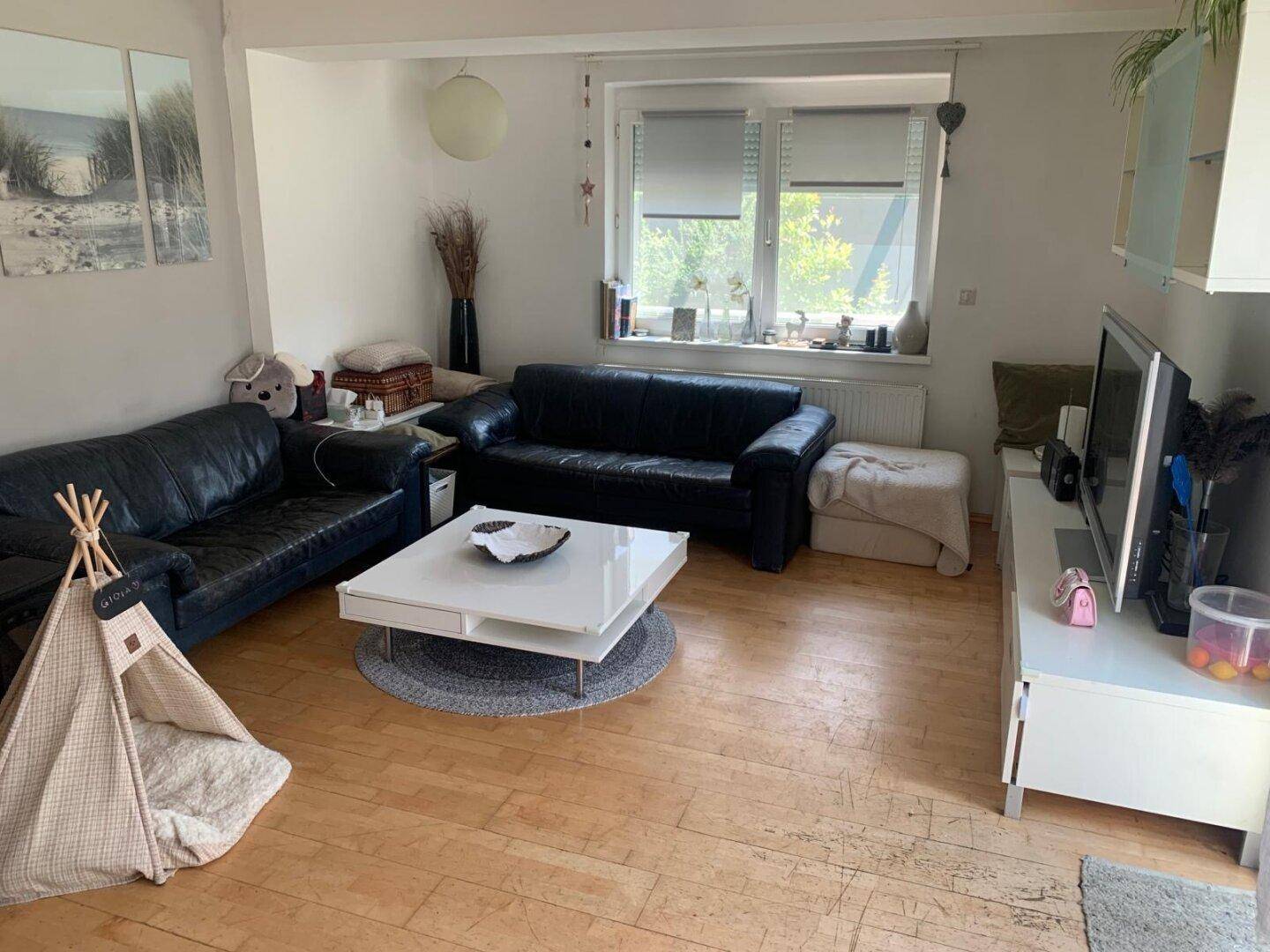 Geräumiges Wohnzimmer mit zwei Ledersofas, Couchtisch und Fenster mit Blick nach draußen.