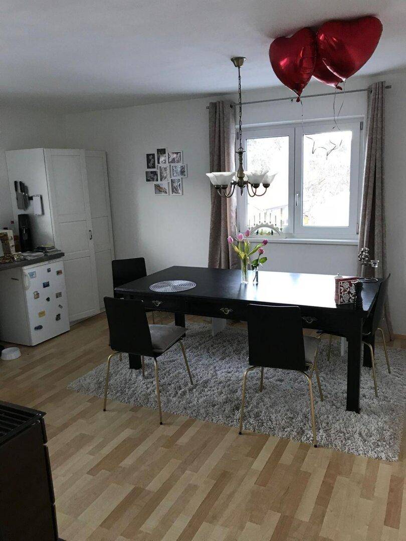 Esszimmer mit großem schwarzem Esstisch, Stühlen und Fenster mit Blick ins Grüne.
