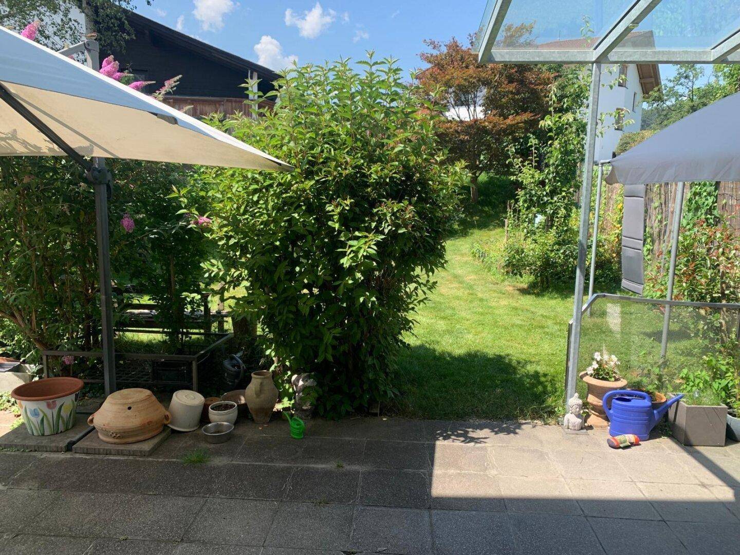 Sonniger Garten mit Terrasse, üppiger Bepflanzung und Blick auf die umliegende Natur.