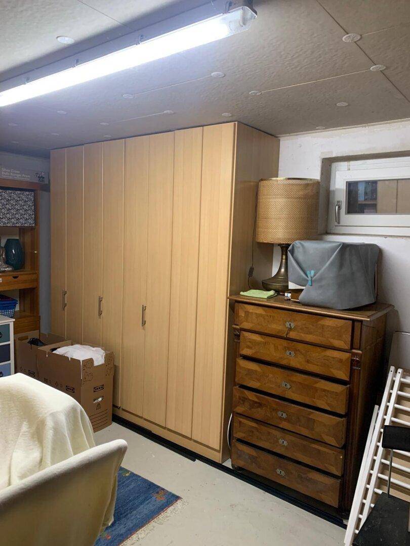 Geräumiger Kellerraum mit Schränken, Kommode und kleinem Fenster, ideal als Abstellfläche.