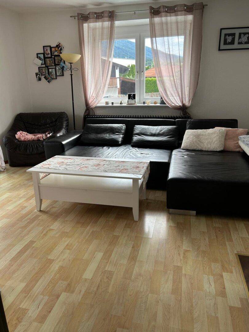 Gemütliches Wohnzimmer mit Ledersofa, Couchtisch und Blick auf die Berge durch das Fenster.