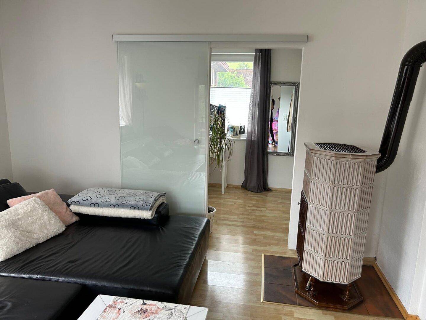 Helles Wohnzimmer mit Kaminofen, bequemer Couch und Blick durch die Glasschiebetür.