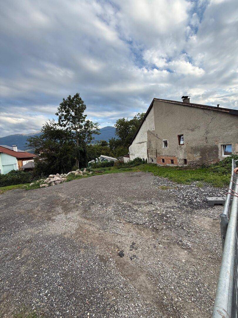 Unbebautes Grundstück neben einem älteren Gebäude mit Putzfassade und Blick auf die umliegenden Berge.