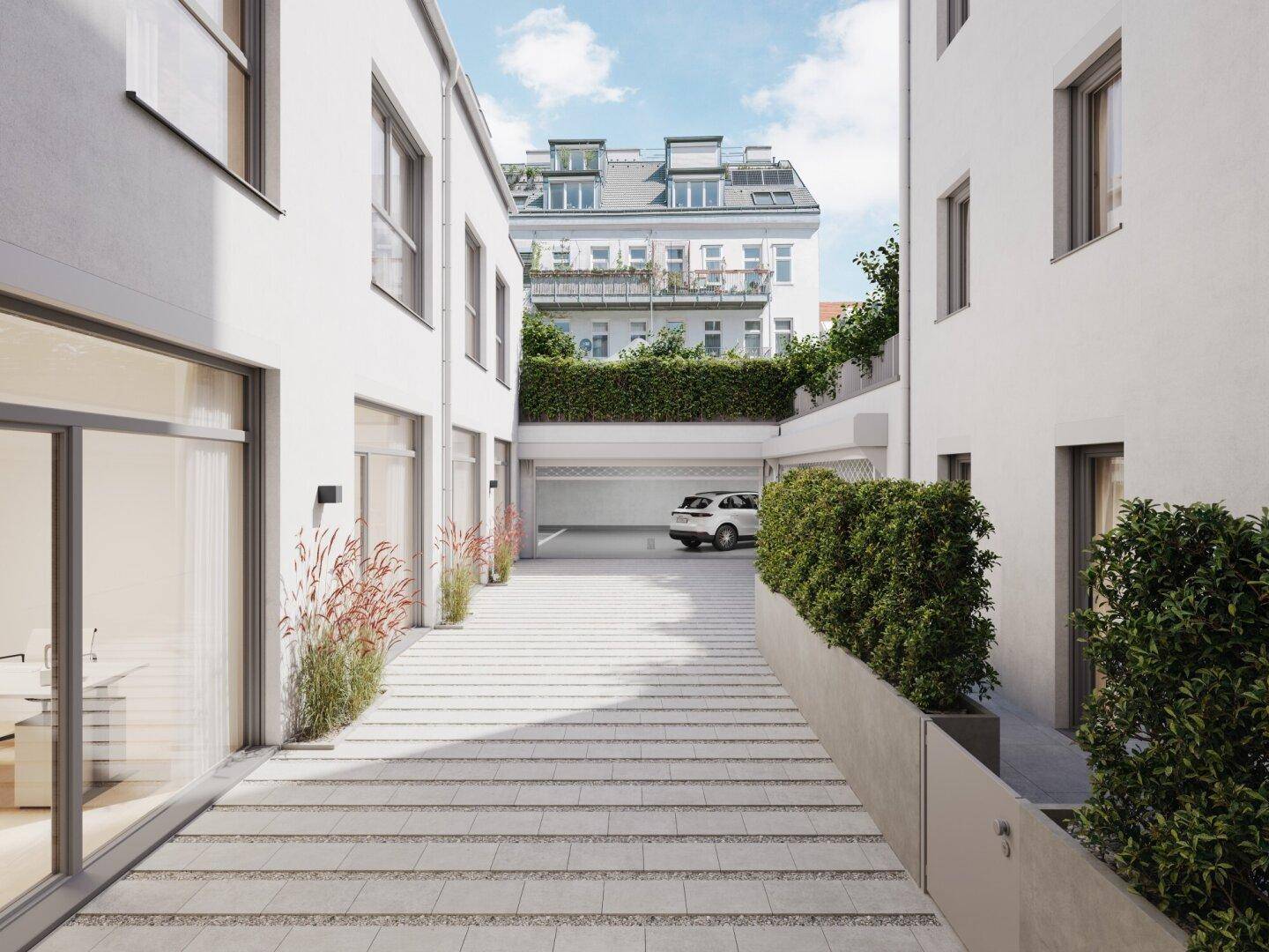 Heller Innenhof mit gepflastertem Weg und Zugang zu einer Tiefgarage, umgeben von modernen Gebäuden.