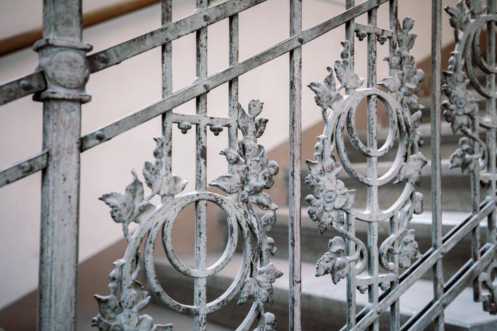Detailaufnahme eines kunstvoll geschmiedeten Treppengeländers mit floralen Ornamenten.