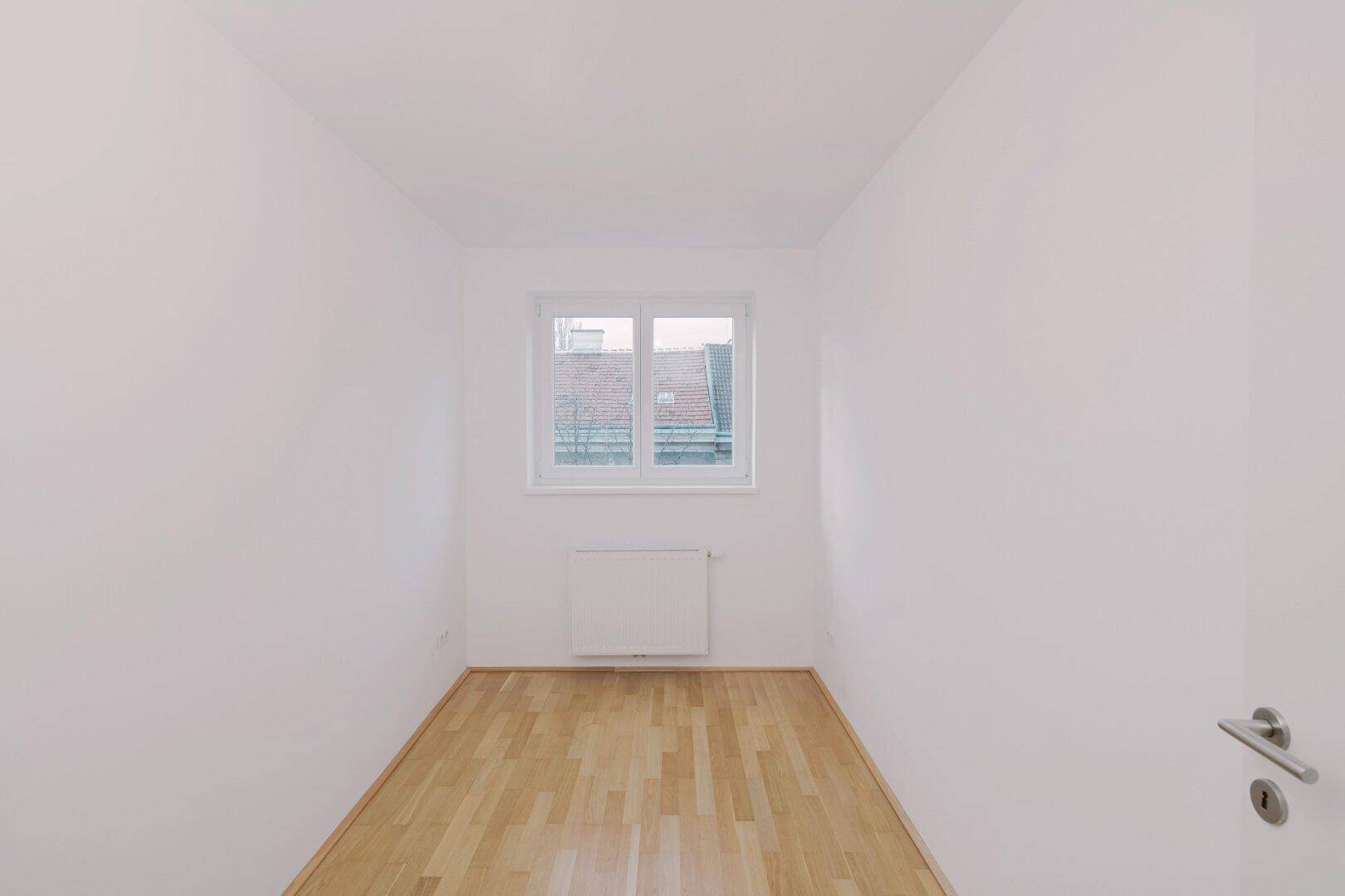 Kleinerer Raum mit Parkettboden, weiß gestrichenen Wänden und einem Fenster.
