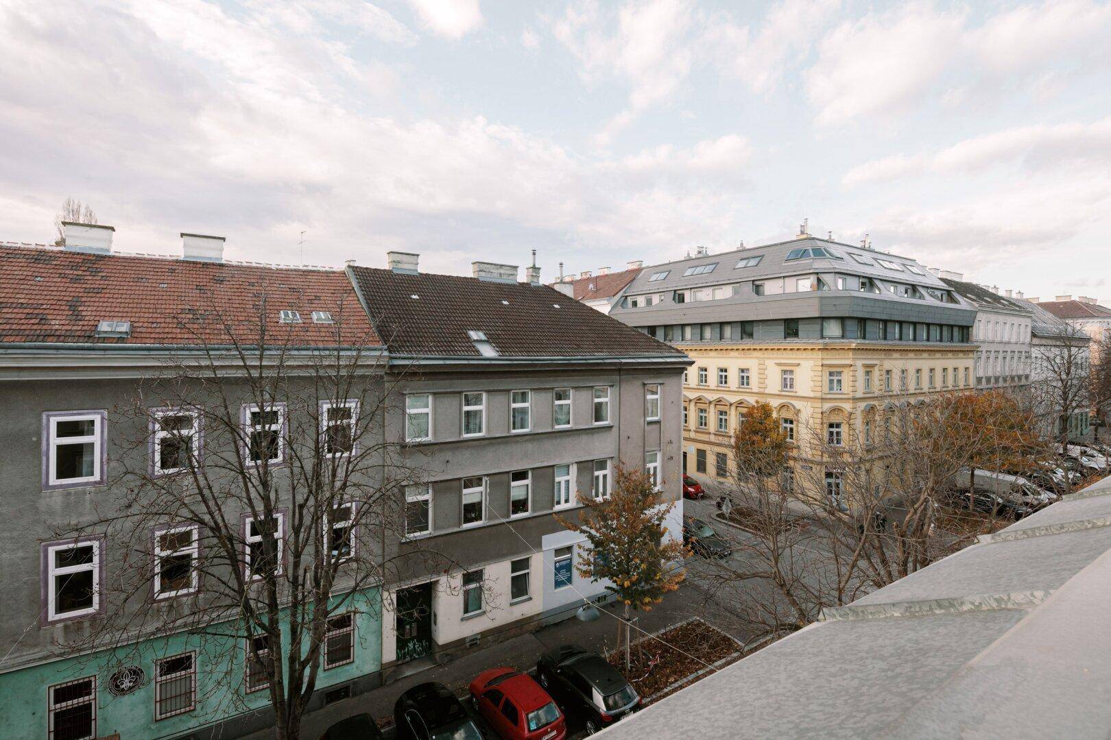 Blick von oben auf eine städtische Straße mit verschiedenen Gebäuden und parkenden Autos.