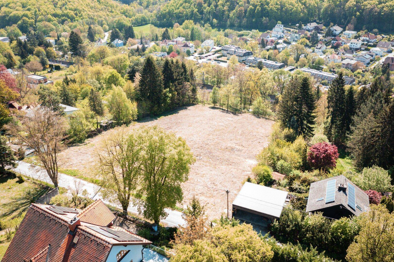 Weitläufige Luftaufnahme eines Baugrundstücks in einer grünen Wohngegend mit vielen Bäumen.