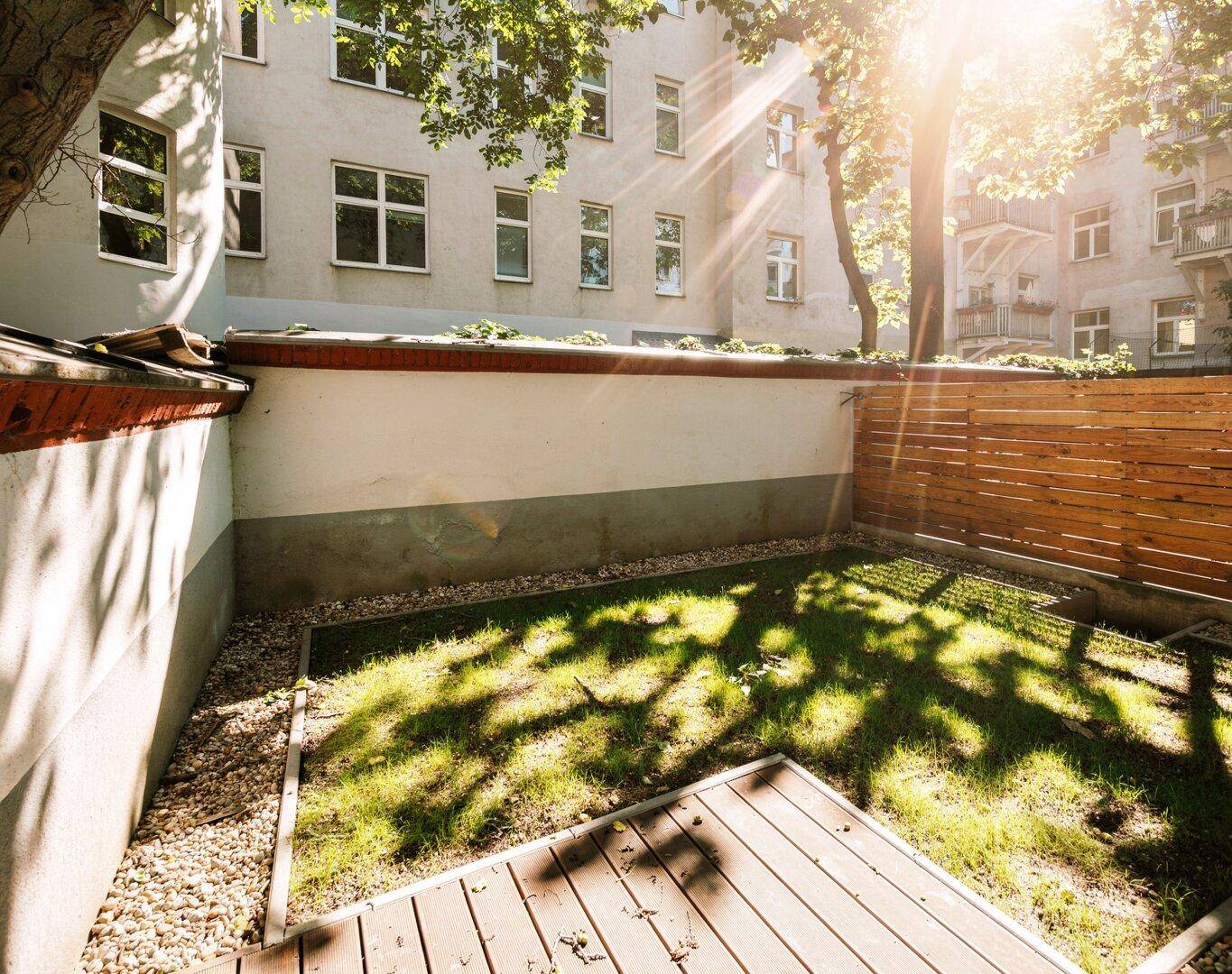 Kleiner, sonniger Gartenbereich mit Holzterrasse und Rasenfläche im Innenhof.