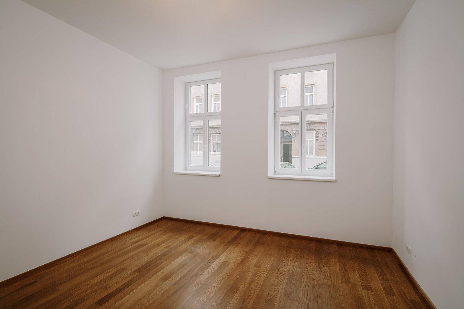 Heller Raum mit zwei großen Fenstern und Holzboden, ideal für Schlaf- oder Wohnbereich.
