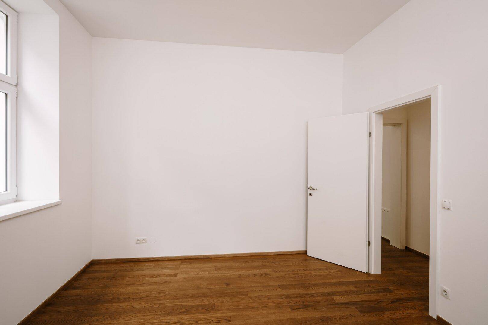 Heller Raum mit Holzboden und einer Tür, die zu einem weiteren Bereich führt.