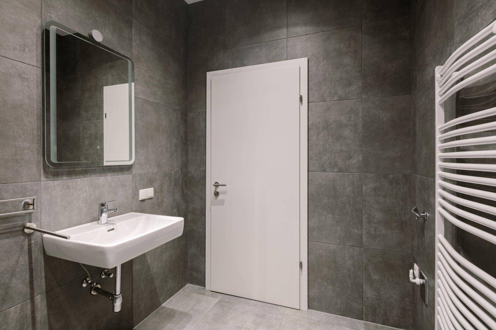 Modernes Badezimmer mit grauen Fliesen, Waschbecken und beheiztem Handtuchhalter.