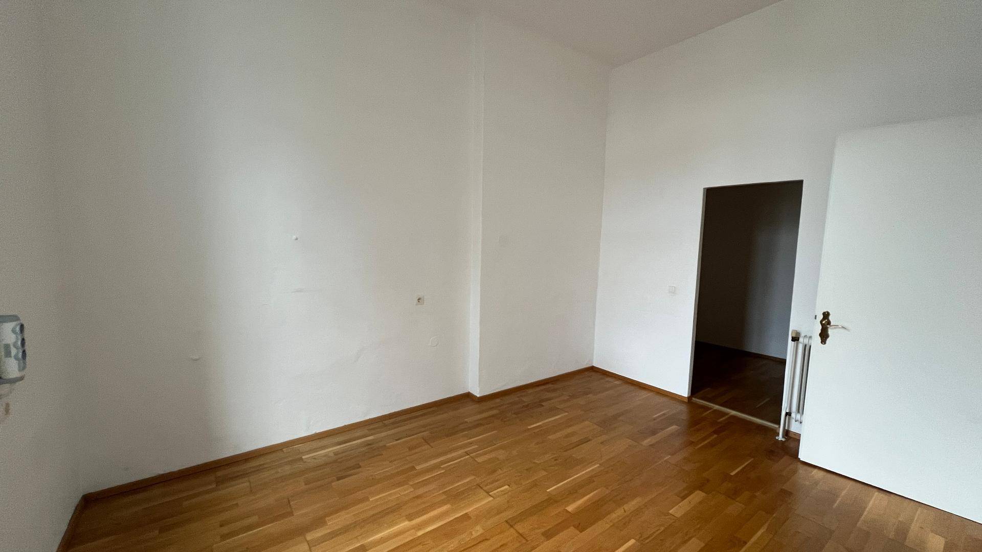 Helles, leeres Zimmer mit Holzparkettboden und weißen Wänden, bereit zur individuellen Gestaltung.