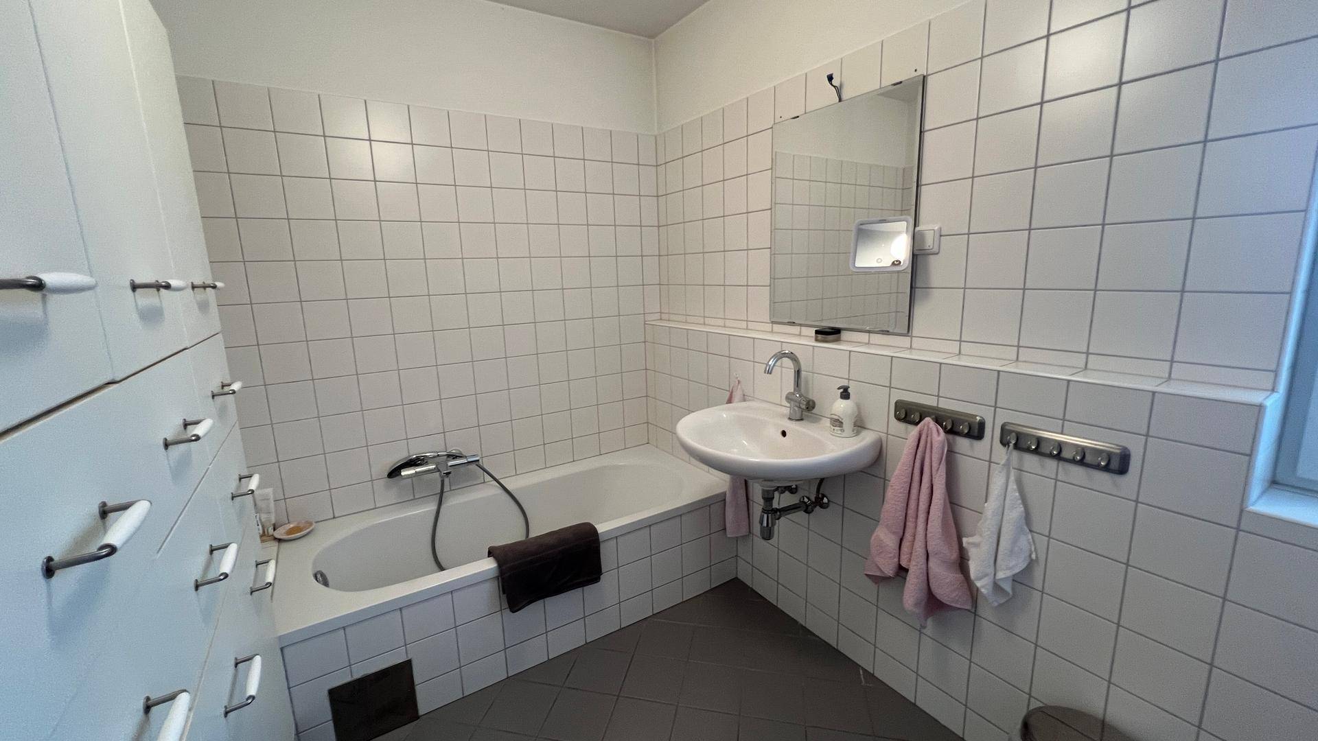 Badezimmer mit Badewanne, Waschbecken und weißen Wandfliesen, praktisch und hell.